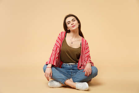 Portrait of tender pretty young woman in casual clothes sitting, looking camera isolated on pastel beige wall background in studio. People sincere emotions, lifestyle concept. Mock up copy spaceの写真素材