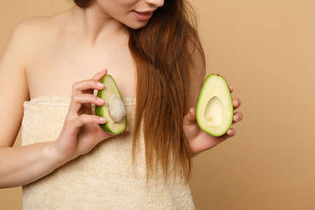 Close up brunette half naked woman 20s with perfect skin nude make up hold avocado isolated on beige pastel wall background studio portrait. Healthcare cosmetic procedures concept. Mock up copy spaceの写真素材