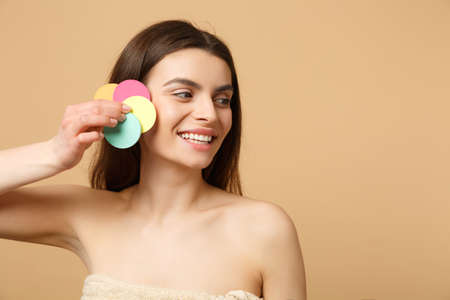 Close up brunette half naked woman 20s with perfect skin, removing nude make up isolated on beige pastel wall background, studio portrait. Health care cosmetic procedures concept. Mock up copy spaceの写真素材