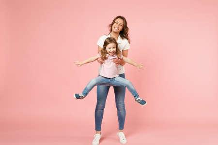 Woman in light clothes have fun with cute child baby girl. Mother, little kid daughter isolated on pastel pink wall background, studio portrait. Mother's Day love family, parenthood childhood conceptの写真素材
