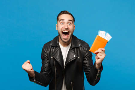 Young happy unshaven man in black jacket white t-shirt hold in hand passport tickets isolated on blue background. Passenger traveling abroad getaway. Air flight journey concept Mock up copy spaceの写真素材