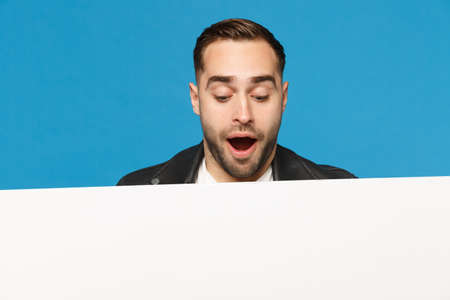 Fun young bearded man look out big white empty blank billboard for promotional content isolated on blue wall background studio portrait. People sincere emotions lifestyle concept. Mock up copy spaceの写真素材