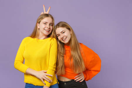 Two smiling young blonde twins sisters girls in vivid colorful clothes having fun, looking camera...