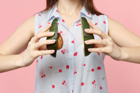 Cropped image young woman in summer clothes hold in hands halfs of fresh ripe avocado fruit isolated on pink pastel wall background. People vivid lifestyle relax vacation concept. Mock up copy spaceの写真素材