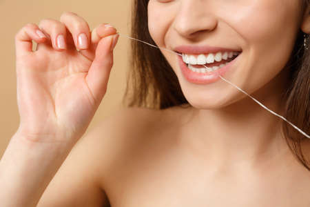 Close up brunette half naked woman 20s with perfect skin nude make up using floss isolated on beige pastel wall background studio portrait. Health care cosmetic procedures concept. Mock up copy spaceの写真素材