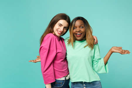 Two young women friends european and african american in pink green clothes standing posing isolated...