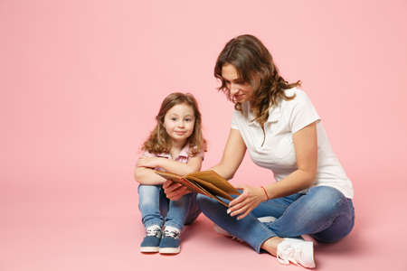 Woman in light clothes have fun read book with child baby girl. Mother, little kid daughter isolated on pastel pink background, studio portrait. Mother's Day, love family parenthood childhood conceptの写真素材