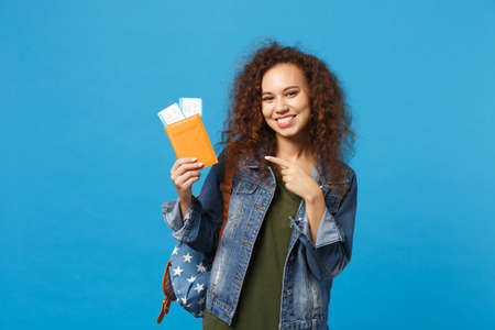 Young african american girl teen student in denim clothes, backpack hold pass isolated on blue wall background studio portrait. Education in high school university college concept. Mock up copy spaceの写真素材