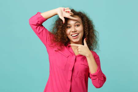 Portrait of cheerful african girl in casual clothes making hands photo frame gesture isolated on blue turquoise background in studio. People sincere emotions lifestyle concept. Mock up copy spaceの写真素材
