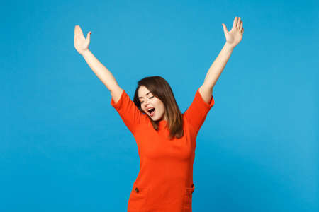 Beautiful excited brunette young woman wearing red orange dress raised hands up winner say Yes...