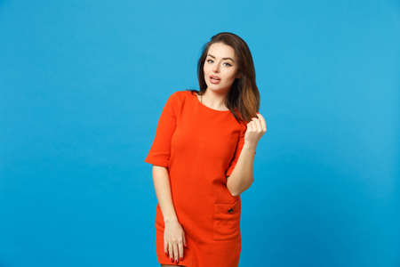 Beautiful brunette young woman wearing red orange dress looking camera standing posing isolated over trendy blue wall background, studio portrait. People lifestyle fashion concept. Mock up copy spaceの写真素材