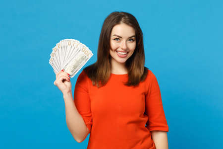 Beautiful brunette young woman wearing red orange dress holding fan of cash money in dollar...