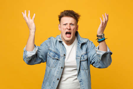 Portrait of irritated screaming young man in denim casual clothes looking camera, spreading hands...