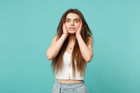 Amazed shocked young woman in light casual clothes looking camera, putting hands on cheeks isolated...