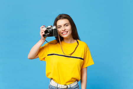 Portrait of smiling young woman in vivid casual clothes take pictures on retro vintage photo camera isolated on bright blue wall background in studio. People lifestyle concept. Mock up copy spaceの写真素材