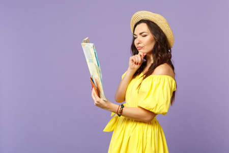 Pensive young woman in yellow dress, summer hat hold city map, passport boarding pass ticket isolated on pastel violet wall background. People sincere emotions, lifestyle concept. Mock up copy spaceの写真素材