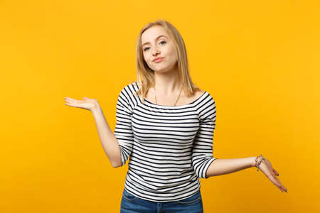 Arrogant haughty young woman in striped clothes spreading, pointing hands aside isolated on yellow orange wall background in studio. People sincere emotions, lifestyle concept. Mock up copy spaceの写真素材