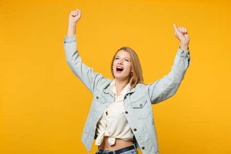 Portrait of happy young woman in denim casual clothes looking aside, doing winner gesture, saying Yes isolated on bright yellow orange wall background. People lifestyle concept. Mock up copy spaceの写真素材