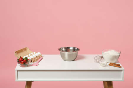 Confectioner baker chef white table with ingredients for cooking cake or cupcake eggs strawberry flour isolated on pink pastel background in studio. Mock up copy space food concept. Nobody interiorの写真素材