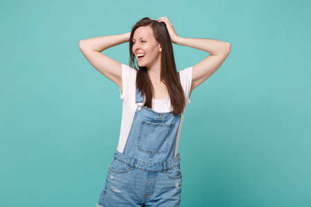 Stunning cheerful young brunette woman girl in casual denim clothes posing isolated on blue turquoise wall background. People lifestyle concept. Mock up copy space. Put hands on head, looking aside.の写真素材
