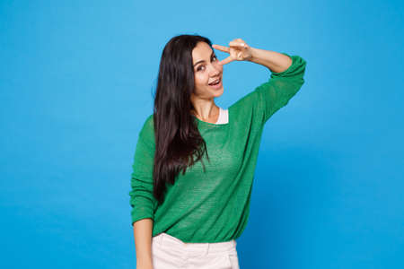 Portrait of cheerful funny young woman in green casual clothes looking camera, showing victory sign...