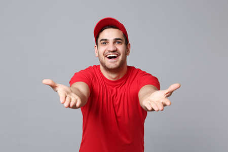 Delivery man in red uniform workwear isolated on grey wall background, studio portrait. Professional male employee in cap t-shirt print working as courier dealer. Service concept. Mock up copy space.の写真素材