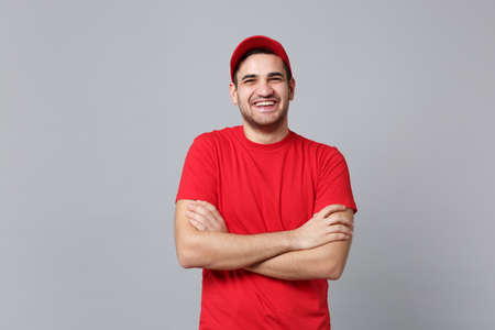 Delivery man in red uniform workwear isolated on grey wall background, studio portrait. Professional male employee in cap t-shirt print working as courier dealer. Service concept. Mock up copy space.の写真素材