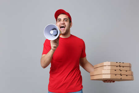 Delivery man giving hold food order pizza boxes isolated on grey background. Professional male pizzaman employee in red cap t-shirt print working as courier dealer. Service concept. Mock up copy spaceの写真素材
