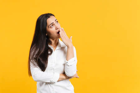 Portrait of boring tired young woman in white casual shirt looking aside covering mouth with hand,...