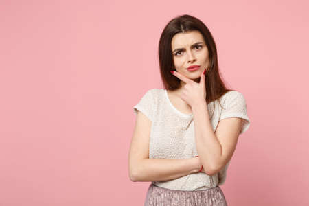 Perplexed pensive young woman in casual light clothes posing isolated on pink wall background,...