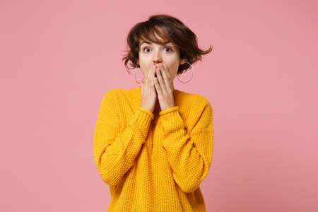 Shocked young brunette woman girl in yellow sweater posing isolated on pastel pink background studio...