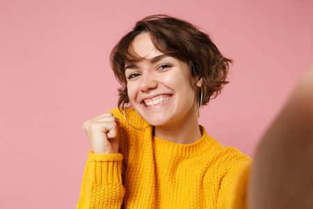 Close up of joyful young brunette woman girl in yellow sweater posing isolated on pink wall...
