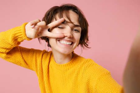Close up of cheerful young woman in yellow sweater posing isolated on pink background. People...