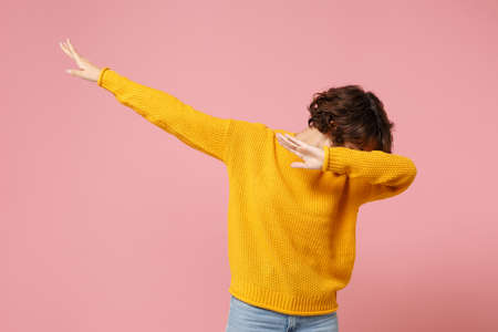 Young brunette woman girl in yellow sweater posing isolated on pastel pink wall background studio portrait. People sincere emotions lifestyle concept. Mock up copy space. Showing DAB dance gesture.の写真素材