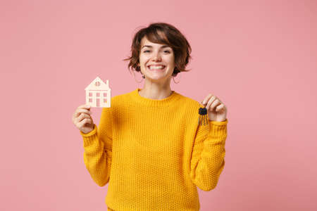 Cheerful young brunette woman girl in yellow sweater posing isolated on pastel pink wall background studio portrait. People lifestyle concept. Mock up copy space. Holding in hands house bunch of keys.の写真素材