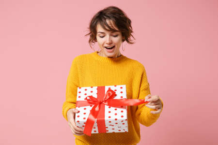 Funny young brunette woman girl in yellow sweater posing isolated on pink background. Valentines Day Womens Day birthday holiday concept. Mock up copy space. Hold present box with gift ribbon bow.の写真素材