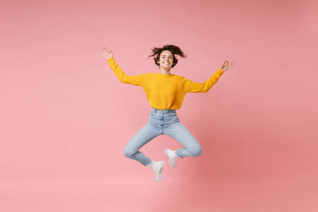 Smiling young brunette woman girl in yellow sweater posing isolated on pastel pink background....