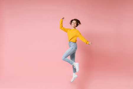 Joyful young brunette woman girl in yellow sweater posing isolated on pastel pink wall background....
