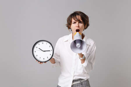 Irritated young business woman in white shirt posing isolated on gray wall background studio...