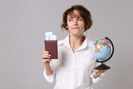 Pensive young business woman in white shirt posing isolated on gray wall background. Achievement career wealth business concept. Mock up copy space. Hold passport, boarding pass, ticket, world globeの写真素材