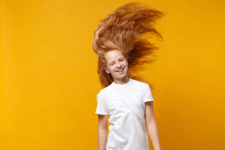 Funny little ginger kid girl 12-13 years old in white t-shirt isolated on yellow background children studio portrait. Childhood lifestyle concept. Mock up copy space. Having fun with fluttering hair.の写真素材