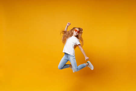 Funny little ginger kid girl 12-13 years old in white t-shirt, heart glasses isolated on yellow wall...