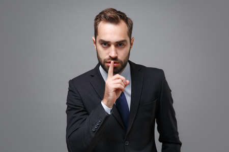 Young business man in classic suit shirt tie posing isolated on grey background. Achievement career wealth business concept. Mock up copy space. Saying hush be quiet with finger on lips shhh gesture.の写真素材