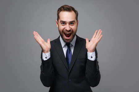 Excited young business man in classic black suit shirt tie posing isolated on grey wall background....