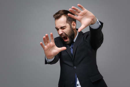 Shocked scared young bearded business man in classic suit shirt tie posing isolated on grey...