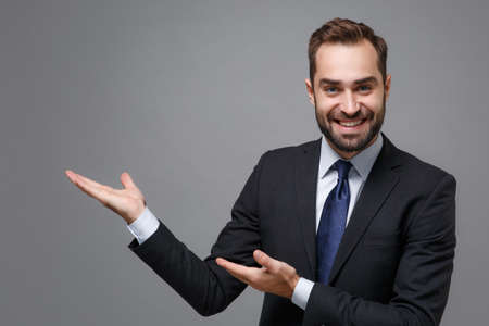 Smiling young bearded business man in classic black suit shirt tie posing isolated on grey...