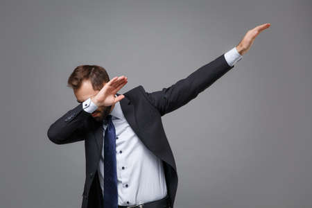 Young bearded business man in classic black suit shirt tie posing isolated on grey background studio portrait. Achievement career wealth business concept. Mock up copy space.Showing DAB dance gesture.の写真素材