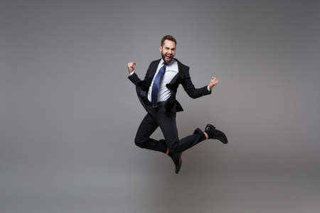 Joyful young business man in classic black suit shirt tie posing isolated on grey background....