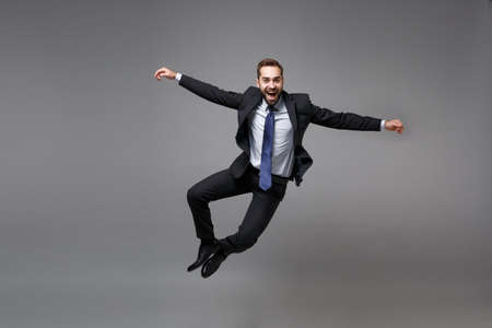Cheerful young business man in classic black suit shirt tie posing isolated on grey background....