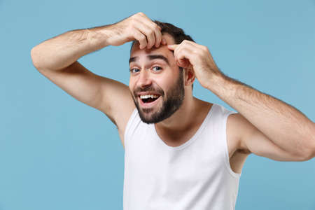 Close up bearded young man 20s years old playing with his face in white shirt isolated on blue pastel background, studio portrait. Skin care healthcare cosmetic procedures concept. Mock up copy space.の写真素材